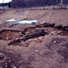 The Daniels house in Waterford during excavation, showing the stone-lined cellar hole that had been buried in a field. Beyond the cellar is a highway entrance ramp  that was built over a colonial-era road. The white tent in the background had been placed over the cellar so it could be excavated in the winter. -  AHS, Inc., Storrs