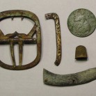 Various personal items from the Goodsell site: a plain brass shoe buckle, a fragment of a silver shoe buckle frame with a repair, a 1746 George II halfpenny, a child's small thimble, and part of a brass jackknife handle with a rococo design - AHS, Inc., Storrs