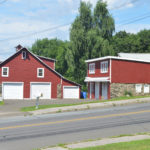 Two buildings next to a road. Both are painted red with garage doors. The foundations appear to be stone.