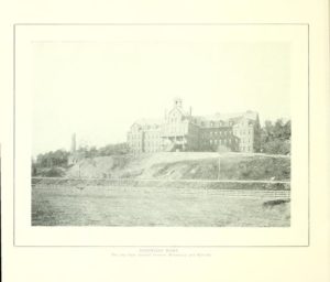 A faded picture of a large institutional building on top of a hill. There is a fence below the hill in the foreground.