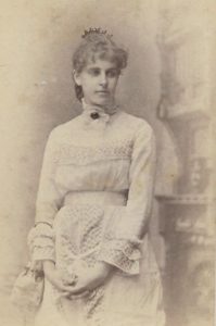 A black and white portrait of a woman in a light colored dress. She is looking down and away from the viewer.