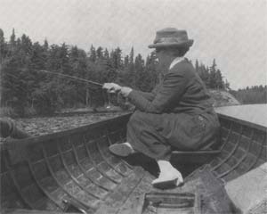 Woman sitting in a small boat on a body of water with a fishing pole in her hand.