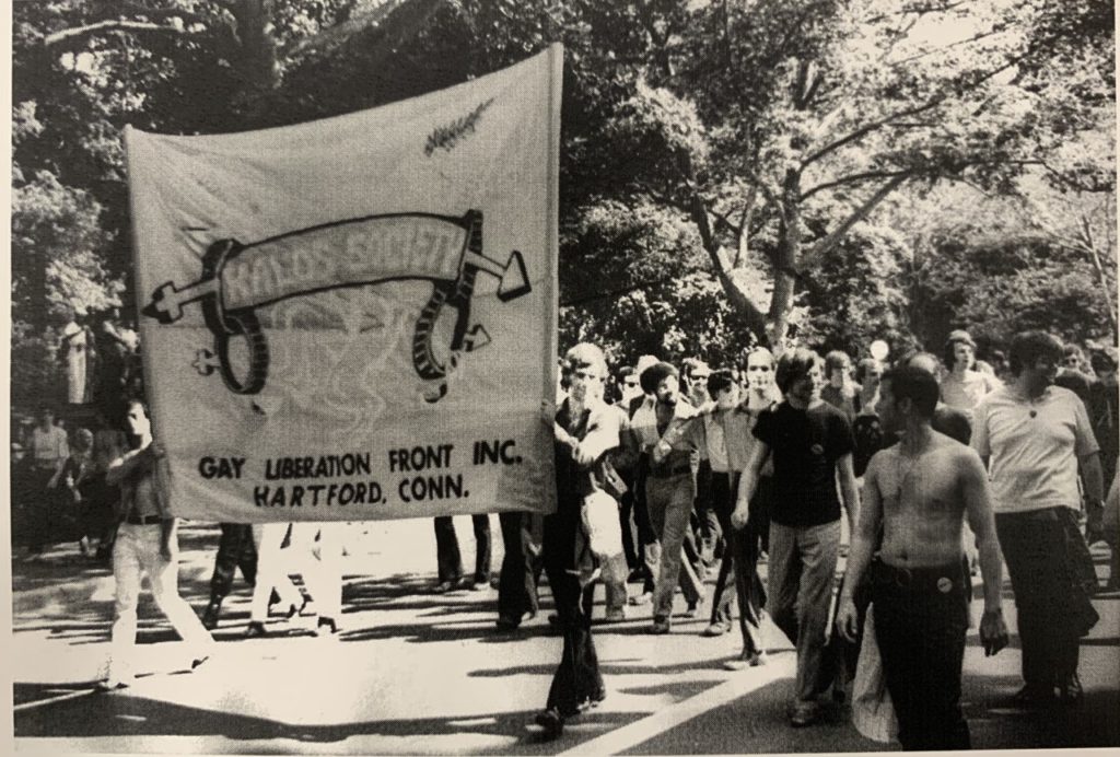 Black and white photo of a group of people. Two people are holding a large banner that says "Kalos Society"