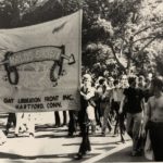 Black and white photo of a group of people. Two people are holding a large banner that says "Kalos Society"