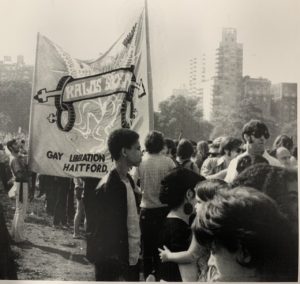 A gathering of a group of people. There is a large banner that reads "Kalos Society". There are large buildings in the background.