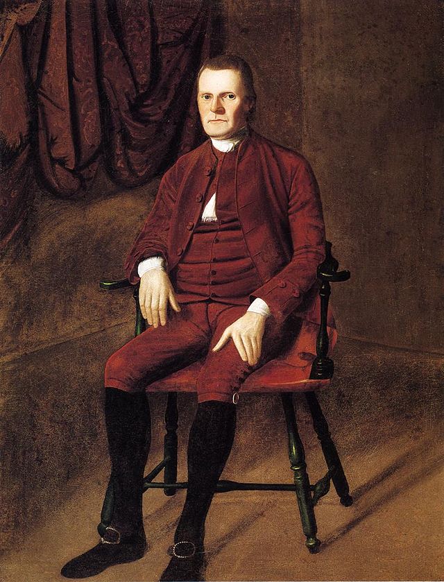 Painting of a man sitting in a chair. There is a drapery behind him. He is wearing a reddish brown suit from the 18th century