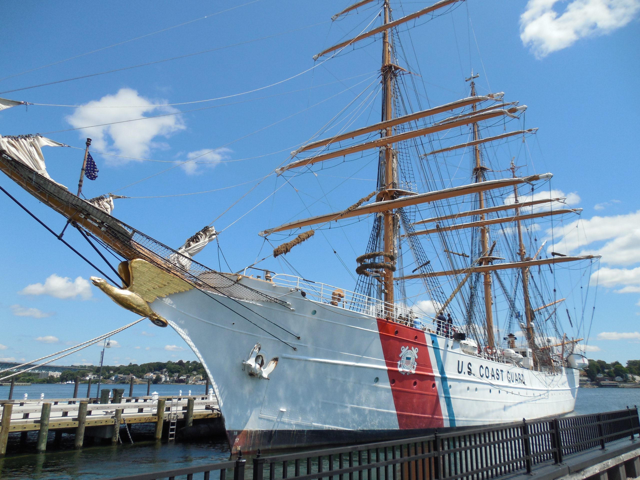 Large white sail boat with three masts next to a dock. It is labeled "US Coast Guard" on the side.