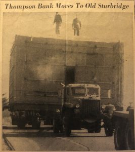 Newspaper clipping of a large box on the back of a truck with two men standing on top of the box.