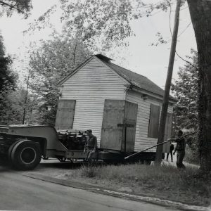 A small building on the back of a trailer. Two men are walking beside the building