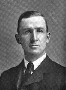 Black and white portrait of a man wearing a suit. He has short hair and is clean shaven