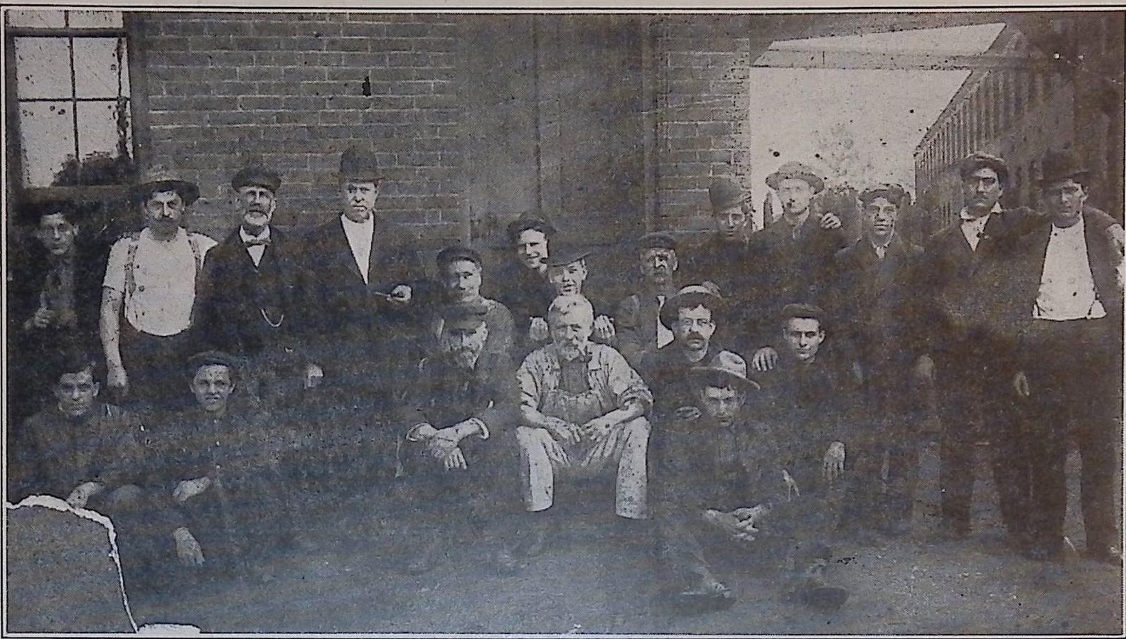 Black and white photograph of a group of men sitting or standing in front of a brick building