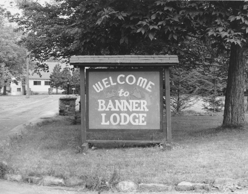 Wooden sign in front of a tree reading "welcome to Banner Lodge"