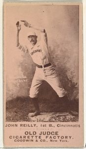 Baseball card with a photograph of a man dressed in a baseball uniform one one foot with his hands in the air above his head. There is text at the bottom.