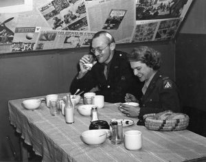 A man and a woman sitting at a table eating and drinking. Both people are wearing military uniforms.