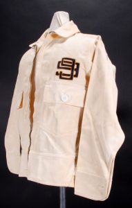 Cream colored flying jacket with a dark colored embroidered emblem on the chest with two intertwined nines