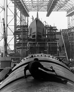 Man sitting on top of a partially constructed submarine in a ship bay