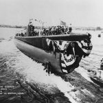 Black and white photograph of a submarine draped in American flags on the water.