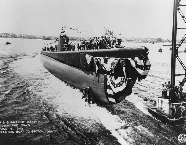 Black and white photograph of a submarine draped in American flags on the water.