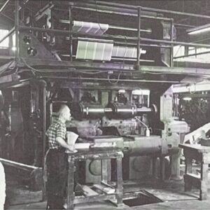 Two people standing next to a large printing press