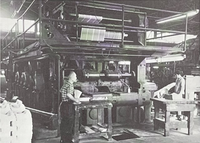 Two people standing next to a large printing press