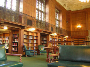 Interior of a wood-paneled library with stacks and a central open space with green leather chairs.