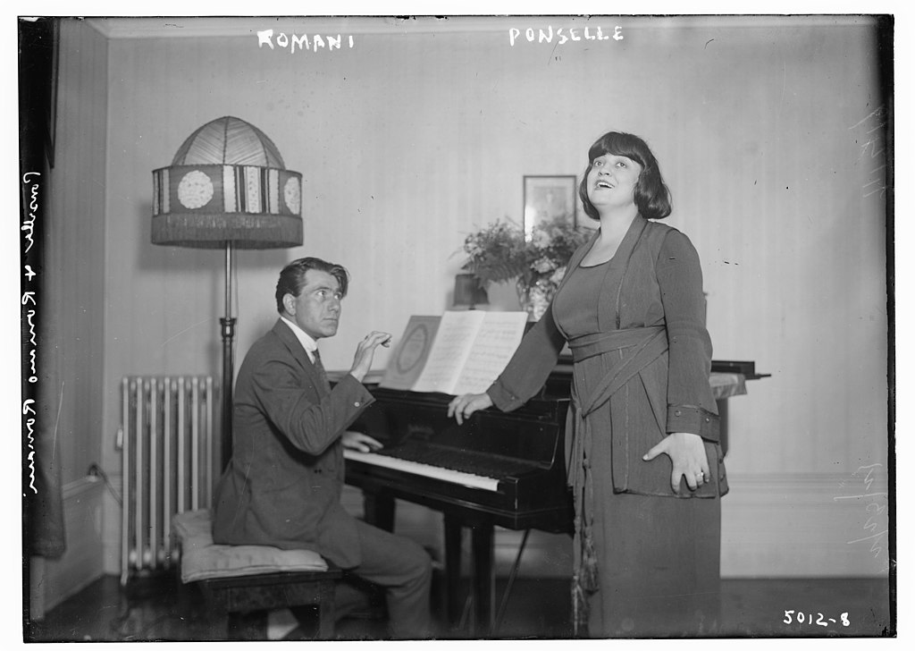 A man sitting at a piano and a woman standing, singing