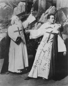 Two men and one woman in a dramatic production. The woman is being held up by one of the men.