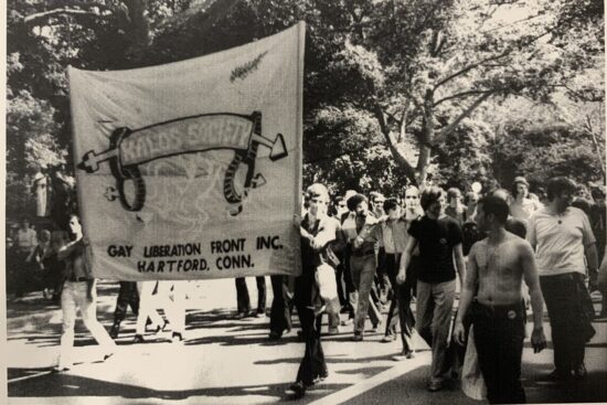 Group of people marching with a large banner that reads "Kalos Society"