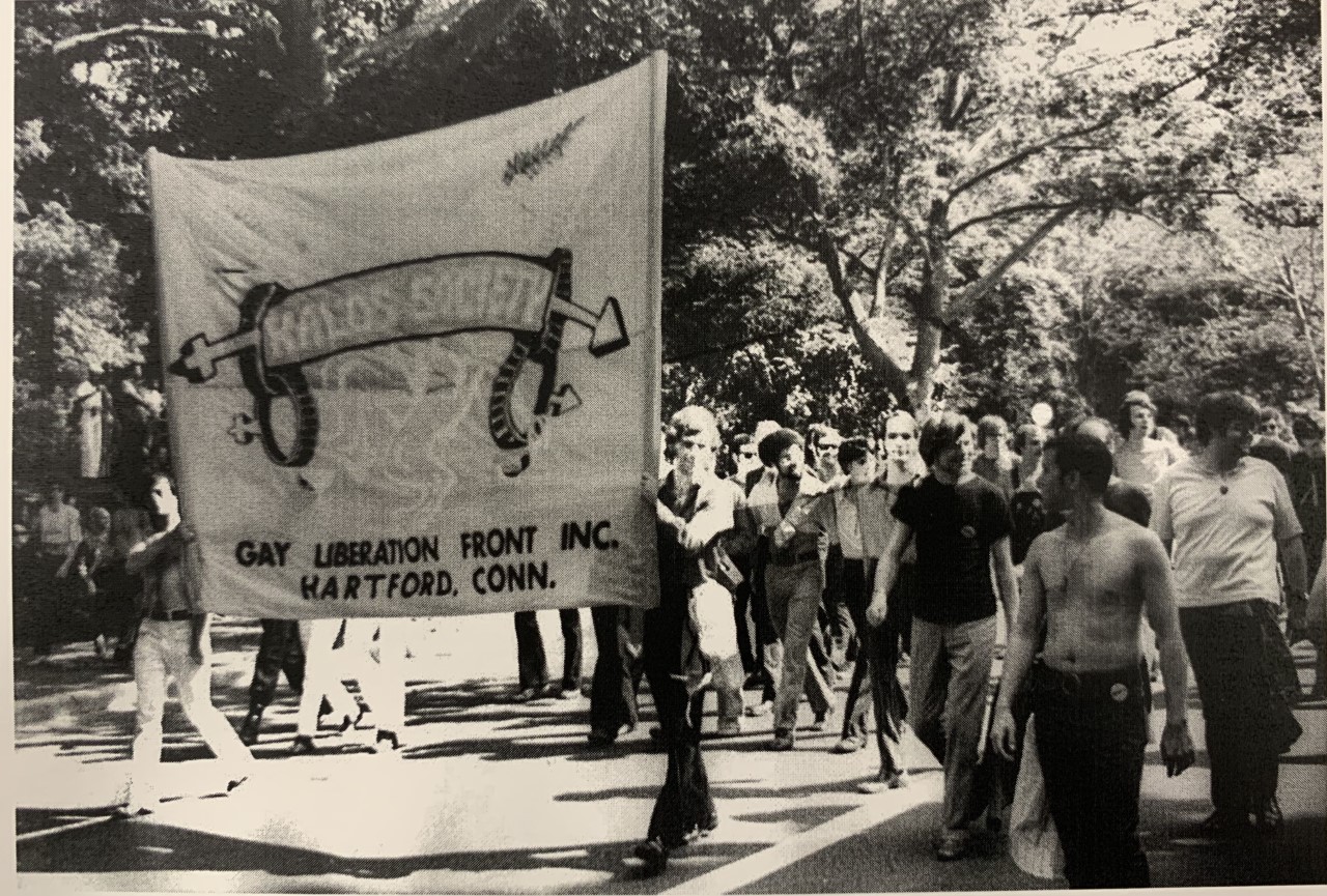 Group of people marching with a large banner that reads "Kalos Society"