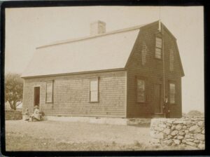 Black and white photograph of a building with a few people in front and on the side