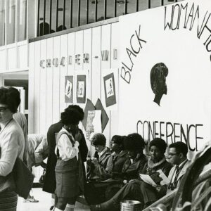 Group of women sitting and standing against a wall with a large banner reading 