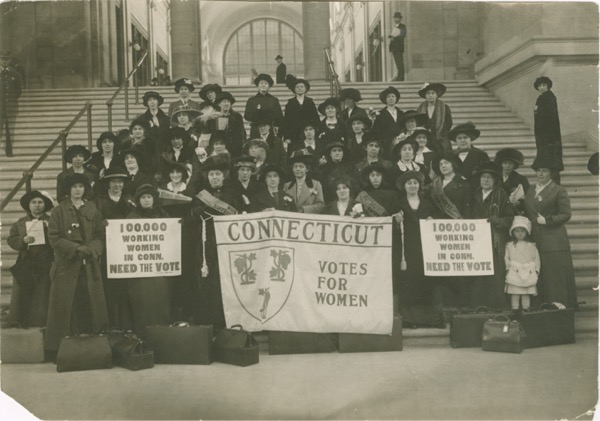 Group of women standing on steps holding banners about women's suffrage