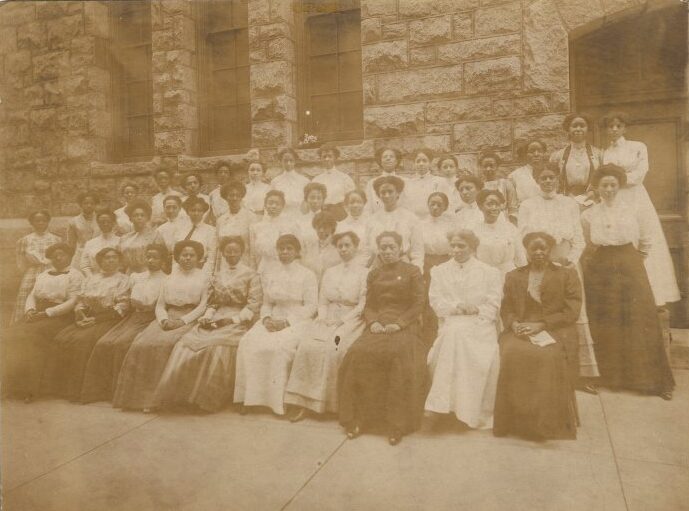 Photograph of a group of seated women in front of a building.