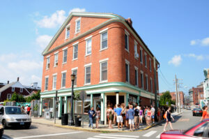 Photograph of a brick building with a line of people outside