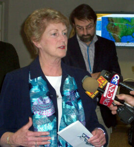 Jodi Rell speaking into a news microphone with a man standing behind her