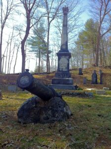Photograph of a cannon in front of a monument in a cemetery