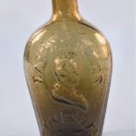 Olive green glass figured flask with a raised profile bust and text.
