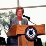 Jodi Rell standing at a podium and speaking into a microphone.