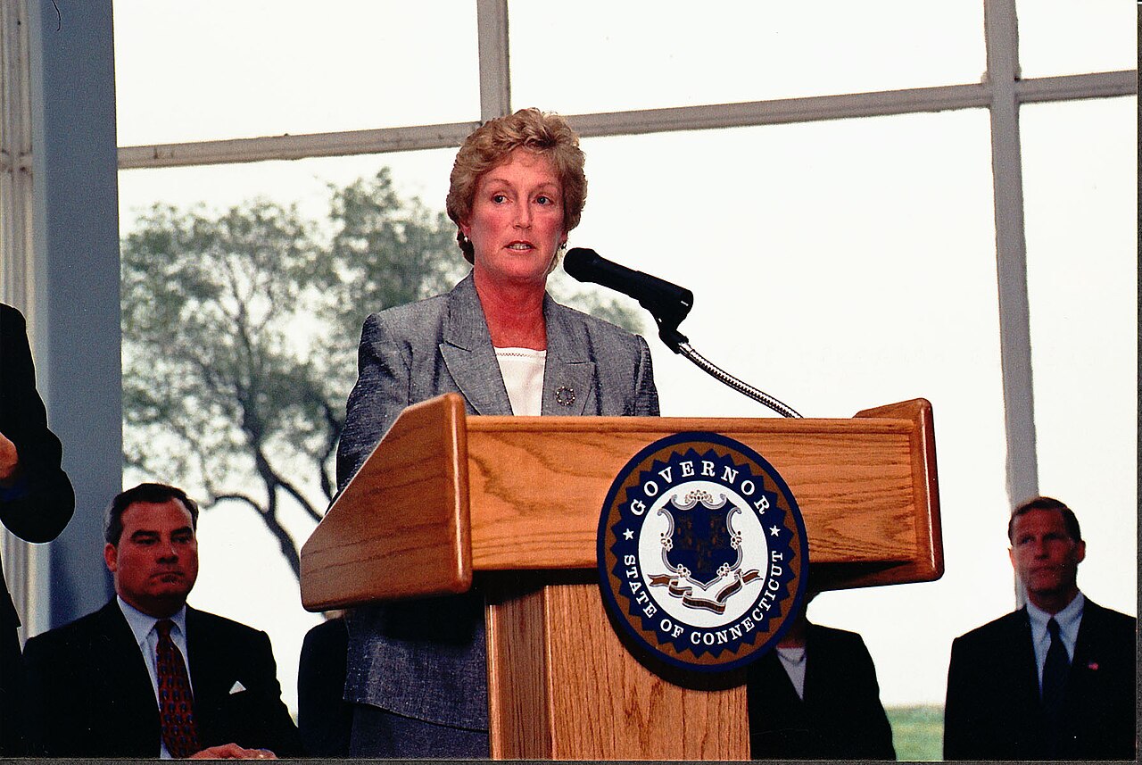 Jodi Rell standing at a podium and speaking into a microphone.